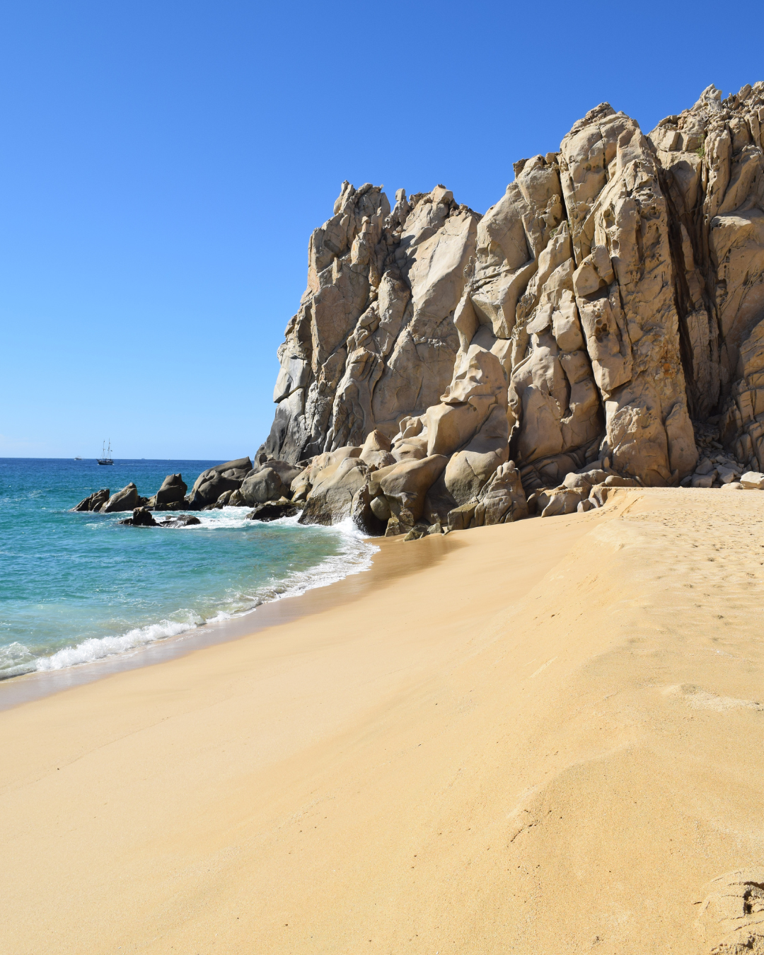 Beautiful sandy beach in Cabo San Lucas with dramatic rocky cliffs and clear blue ocean.