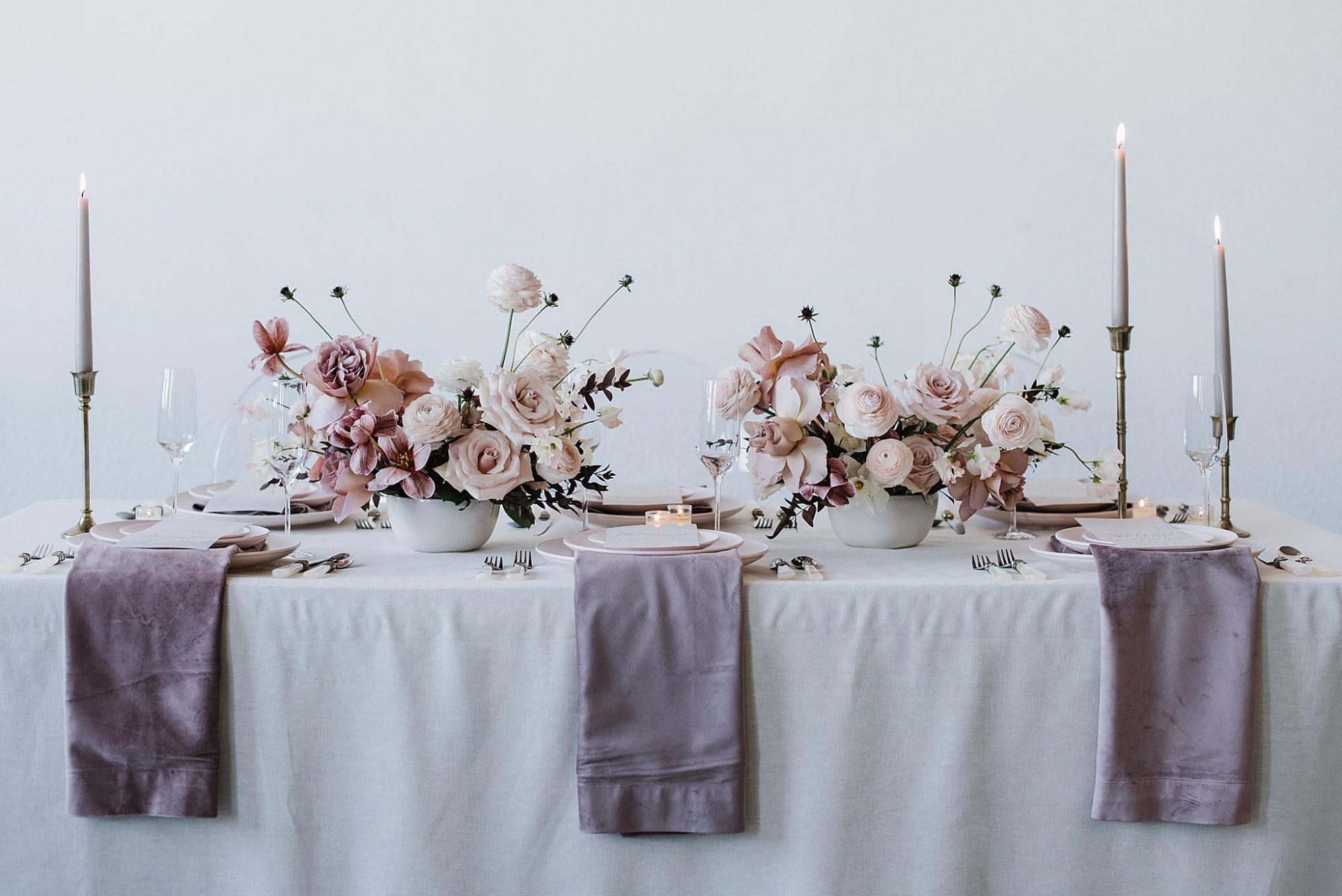 Purple wedding table details. There are blush flowers and white candlesticks.