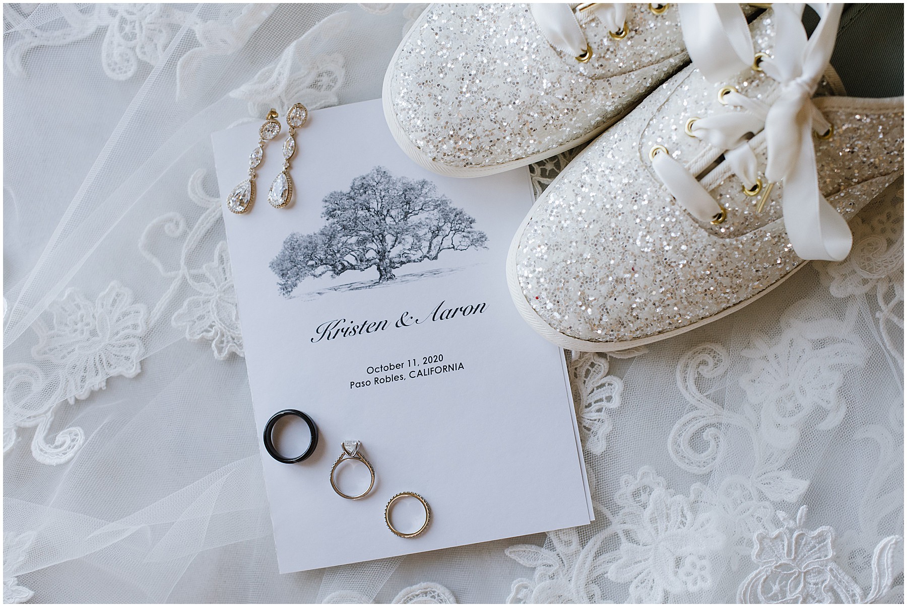 White wedding details. There are white sparkley shoes. They are sitting on a white wedding announcement beneath wedding rings.