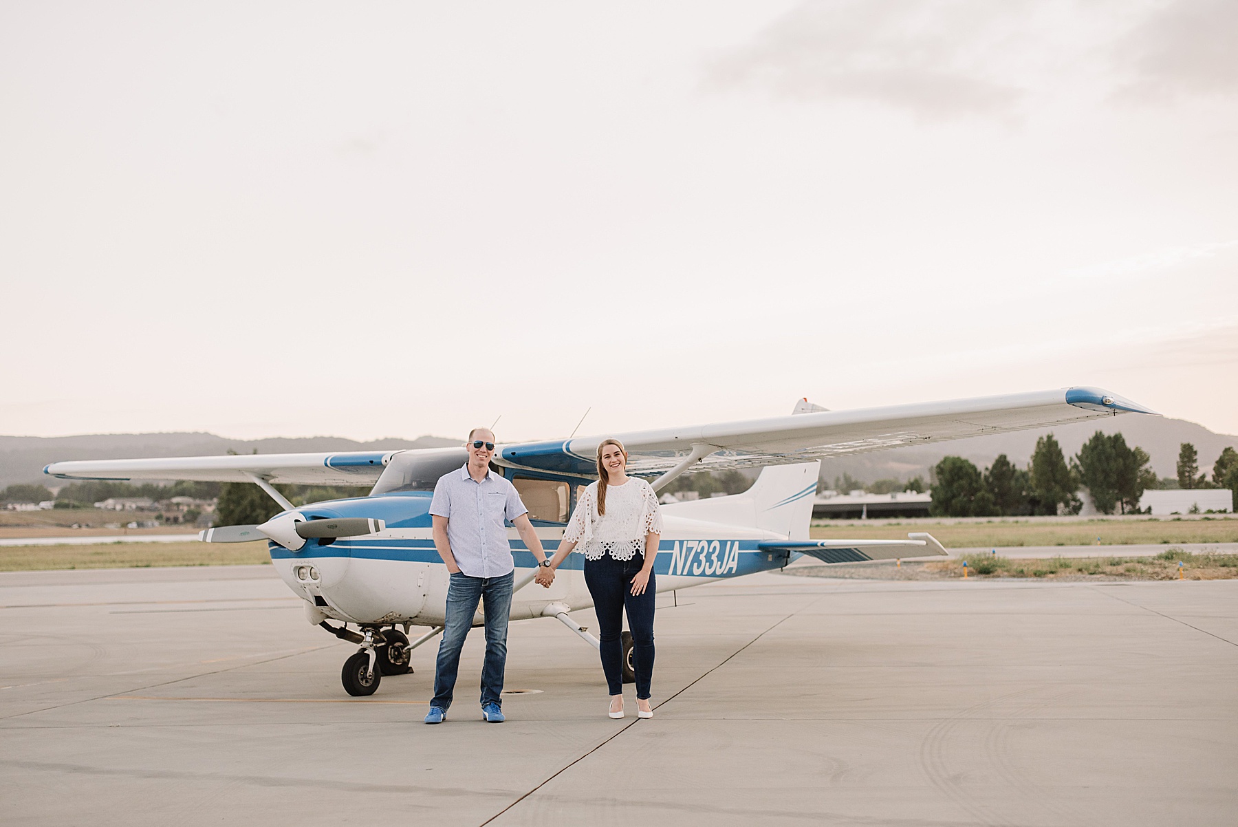 Couple standing hand-in-hand in front of a commuter plane during their SLO engagement session at the San Luis Obispo airport.