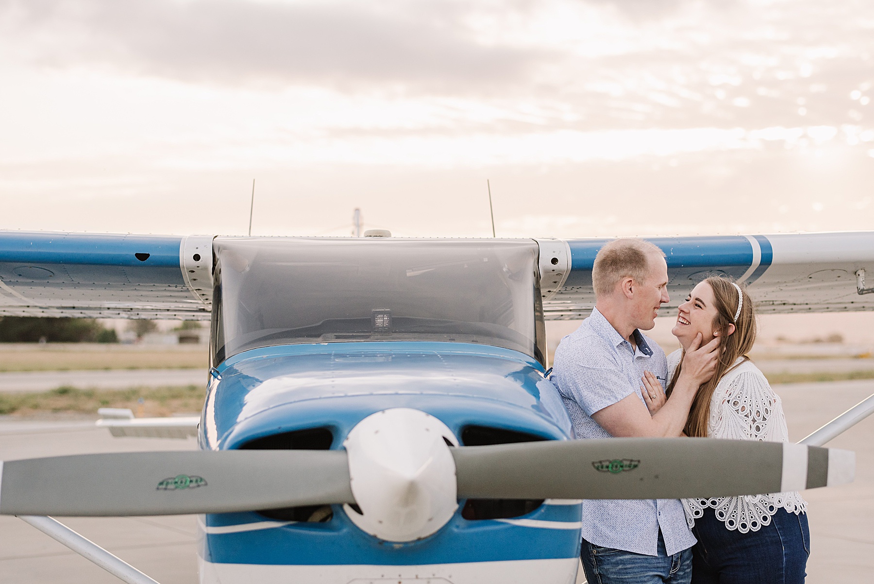 A couple sharing a joyful moment in front of a commuter plane during their SLO engagement session at the San Luis Obispo airport.