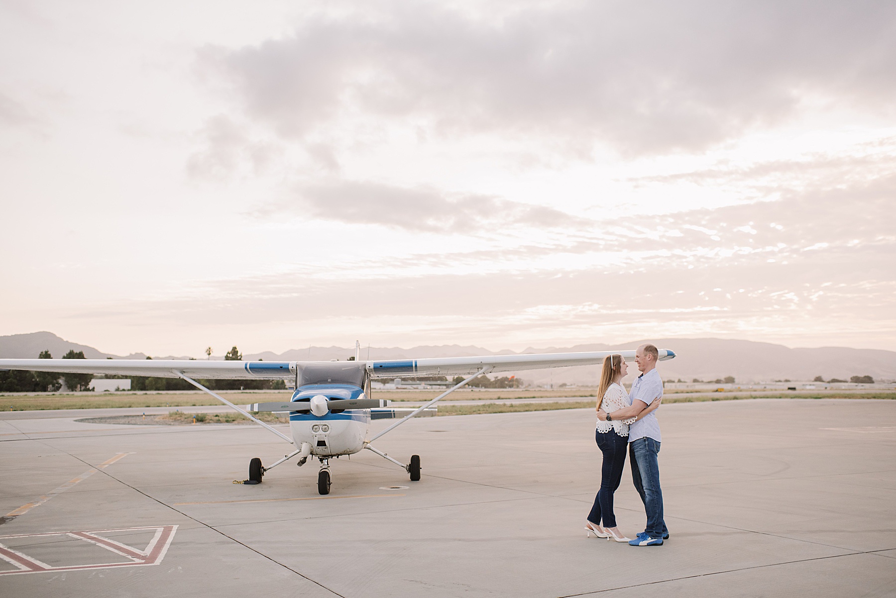 An engaged couple sharing a romantic moment in front of a commuter plane during their SLO engagement session at the San Luis Obispo airport.