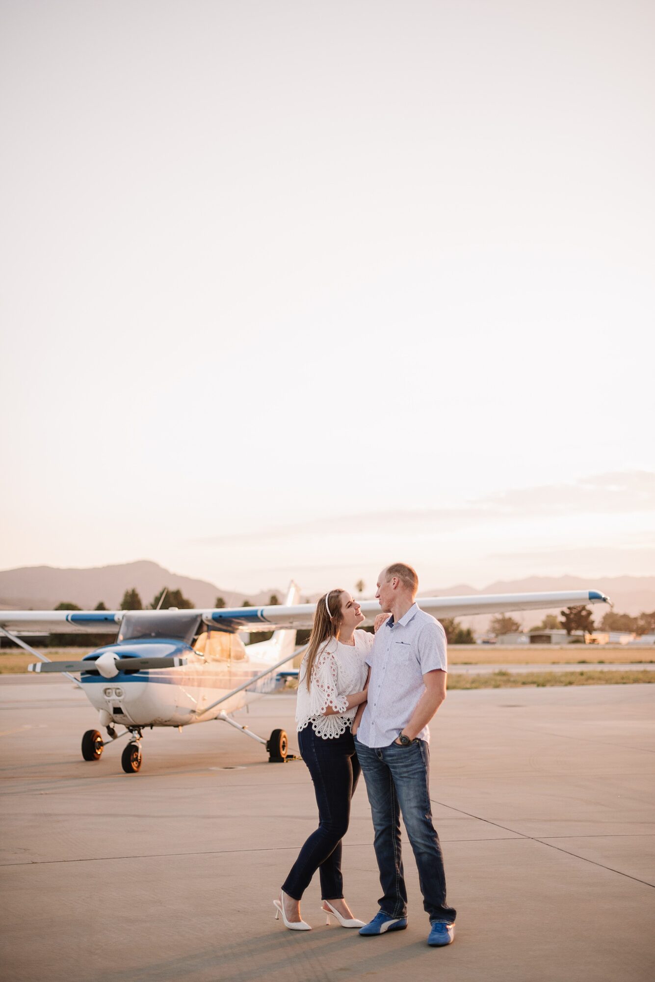 A couple sharing a joyful moment during their SLO engagement session with a commuter plane in the background at the San Luis Obispo airport.