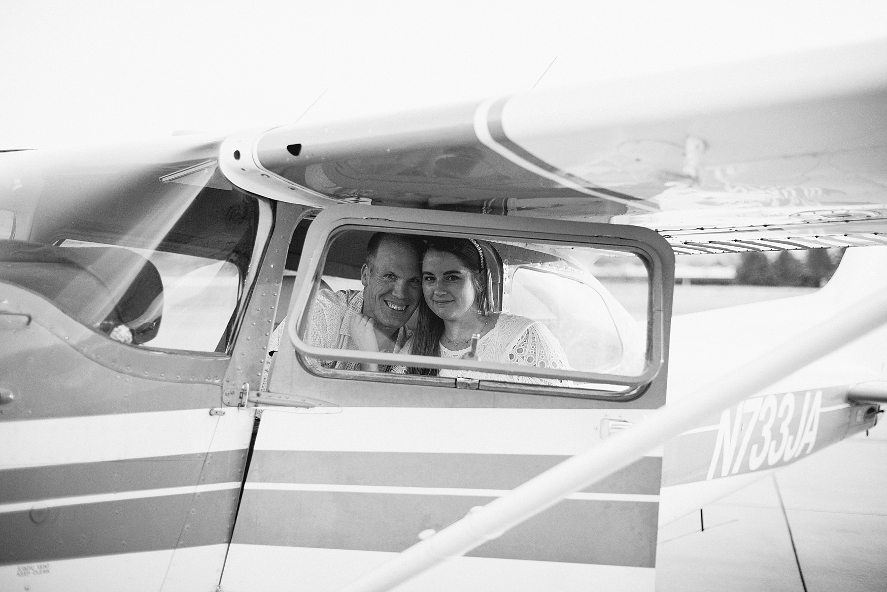 Couple smiling through the window of a commuter plane during their SLO engagement session at the San Luis Obispo airport.