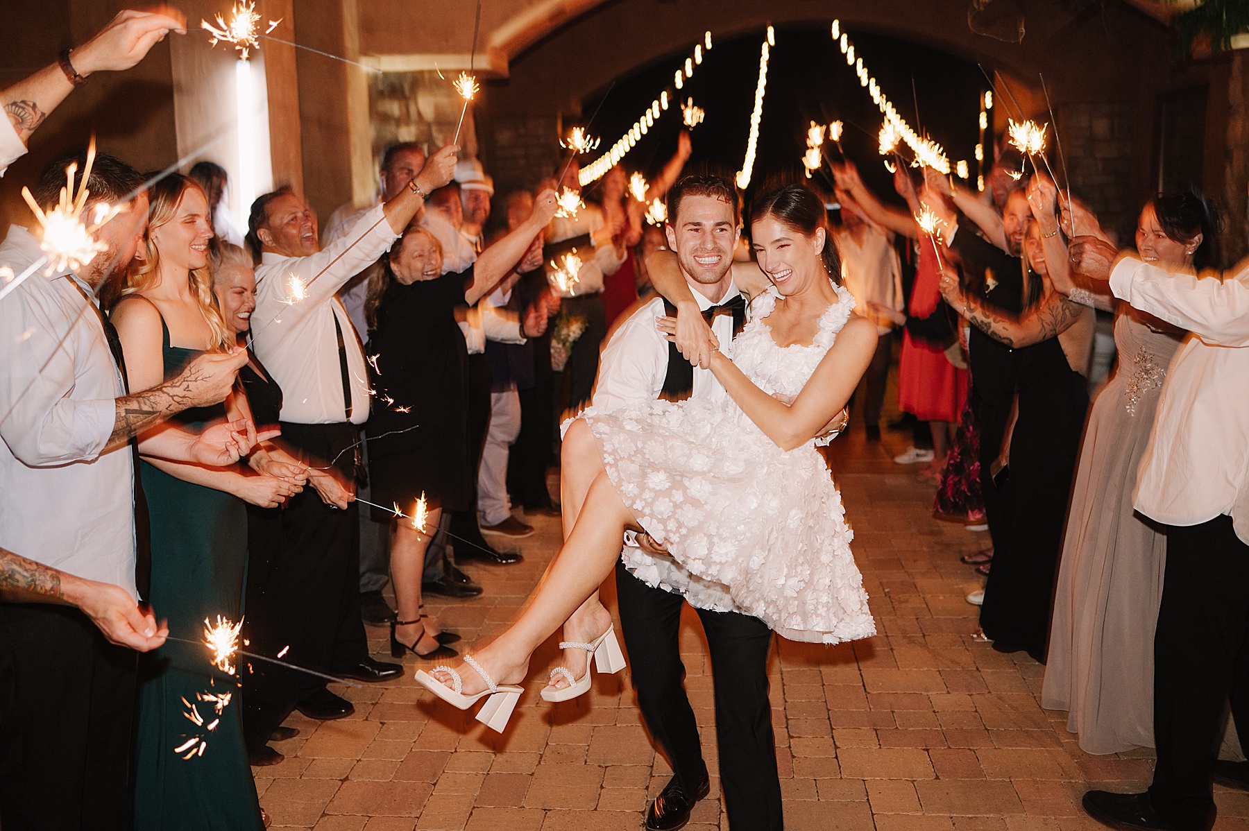 Bride and groom share a joyful sparkler exit surrounded by cheering guests under twinkling lights at Mira Vista Estate, a romantic Tuscan-inspired wedding venue in Paso Robles.