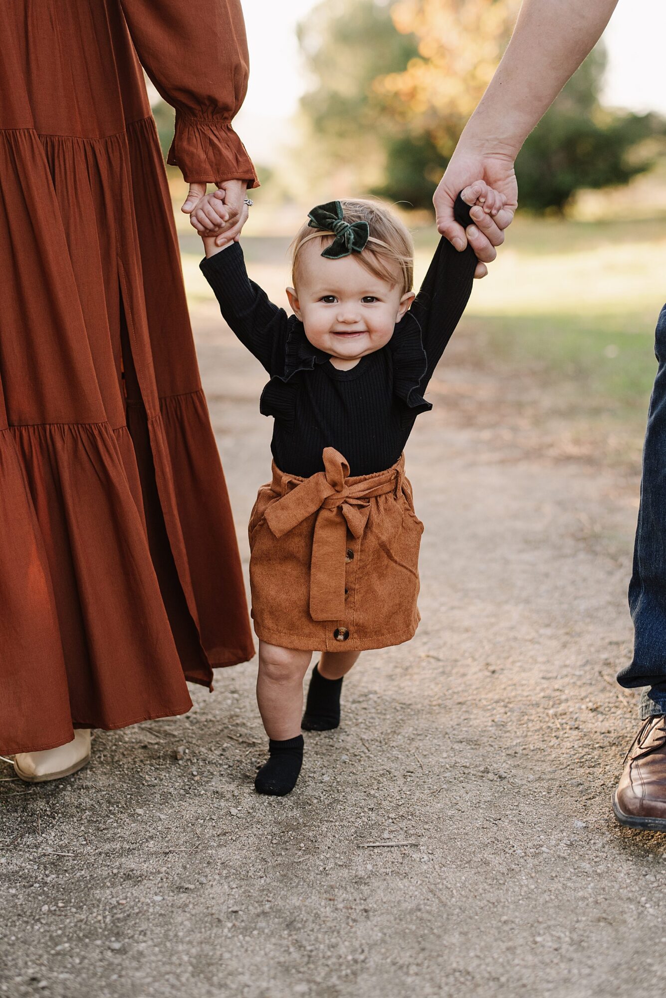 Central Coast family photos of parents and their baby enjoying a fall outdoor session, including a sweet moment of their little one learning to walk.
