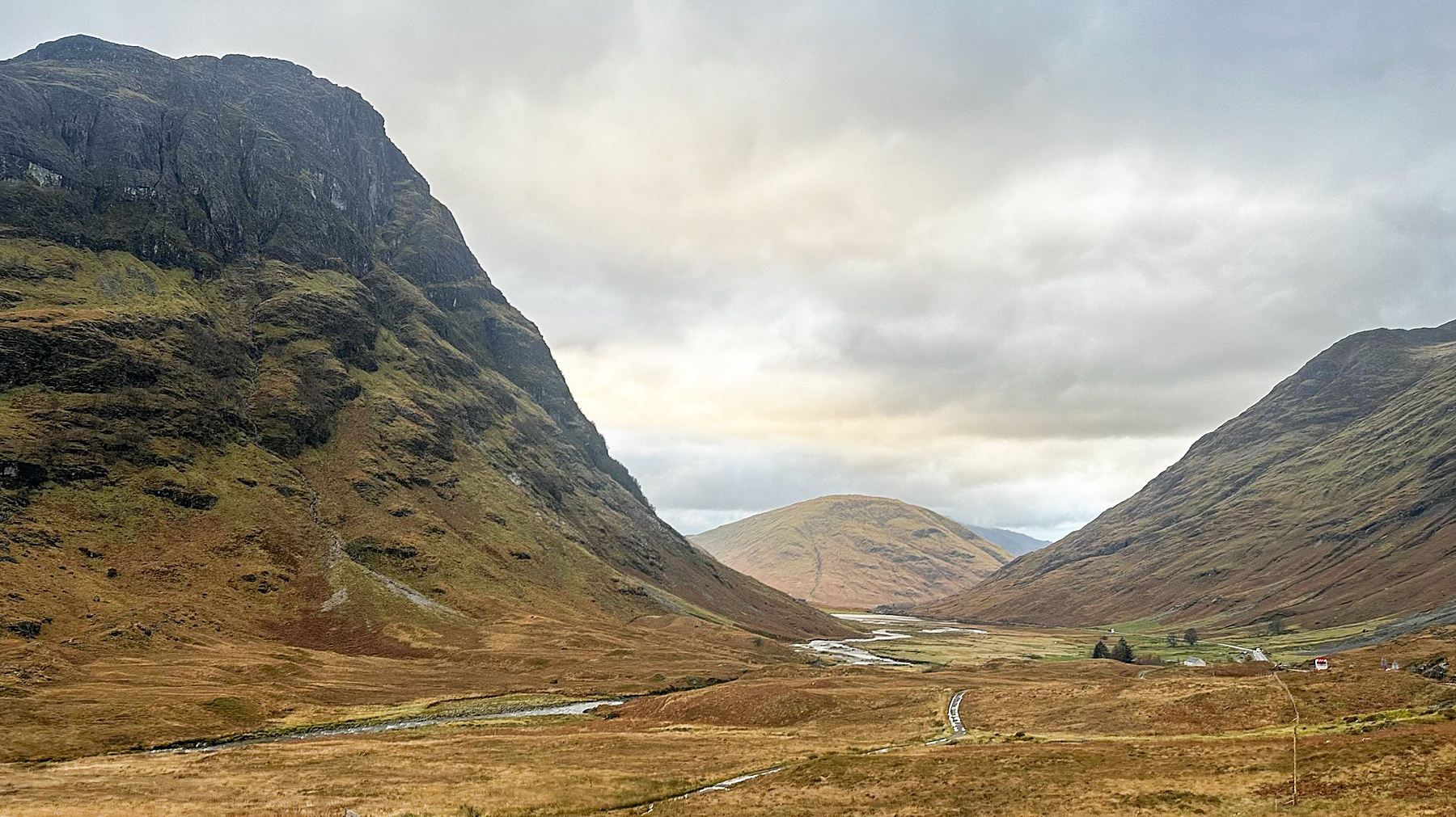 Exploring Scotland through the dramatic Glencoe valley with steep mountain slopes, winding river, and moody overcast skies.