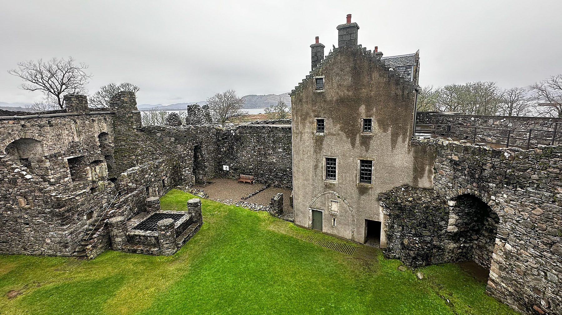 Exploring Scotland at a historic stone castle courtyard with mossy walls, arched doorways, and green grass framed by a cloudy sky.