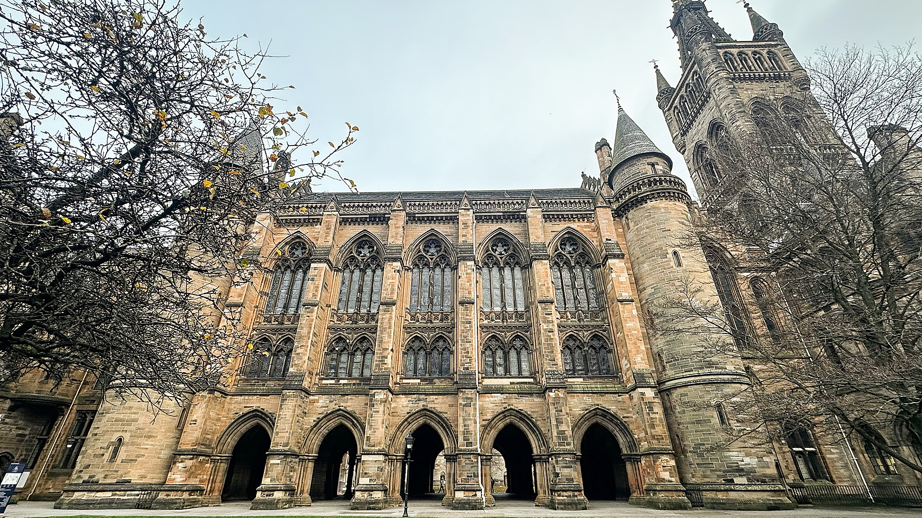 Exploring Scotland at a gothic cathedral facade with tall arched windows, stone towers, and bare autumn branches.
