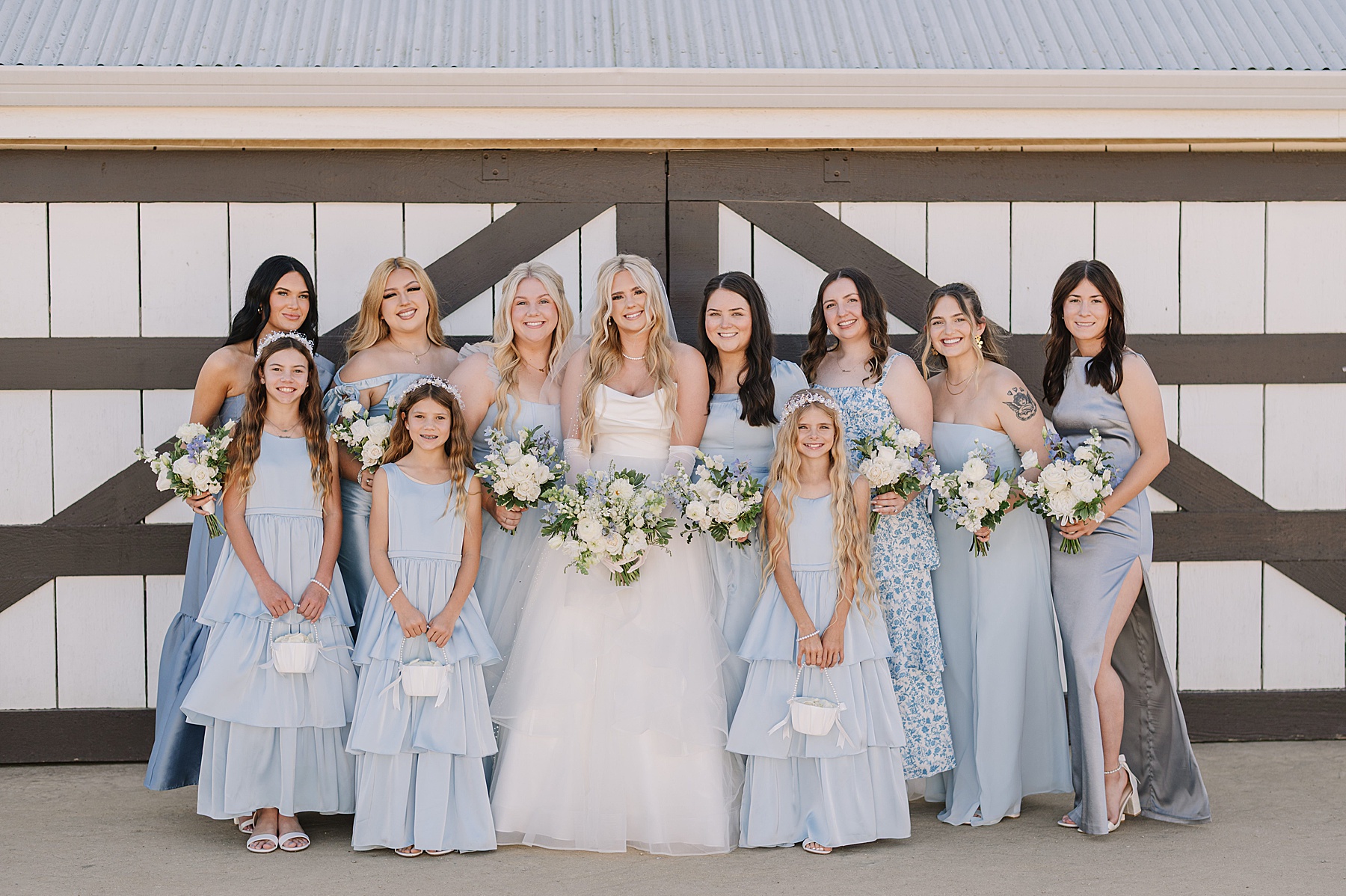Bridal party portraits at White Barn Wedding Venue in Edna Valley, California featuring soft blue bridesmaid dresses, white floral bouquets, and the venue’s iconic white barn backdrop.