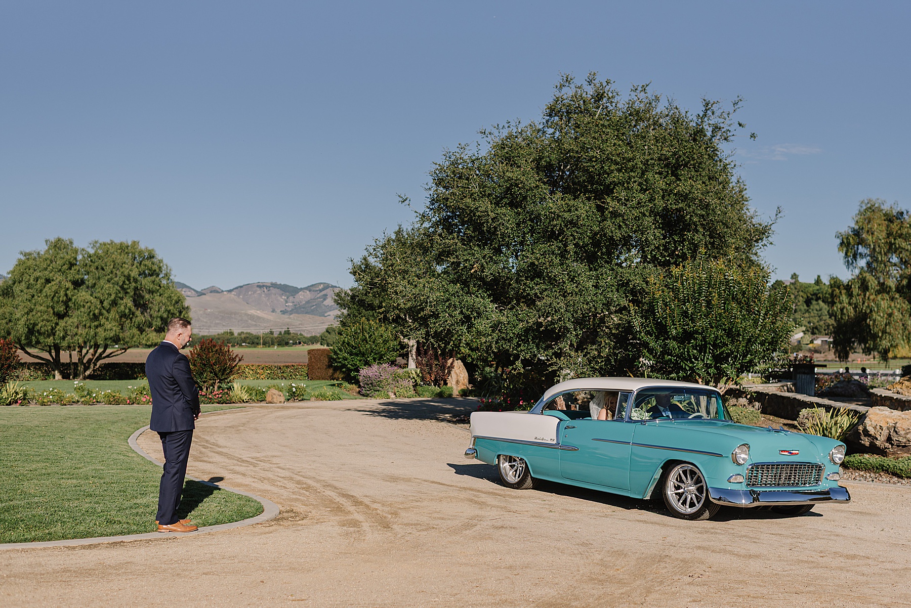Vintage getaway car arriving at White Barn Wedding Venue in Edna Valley, California with scenic vineyard views, oak trees, and classic Central Coast wedding charm.