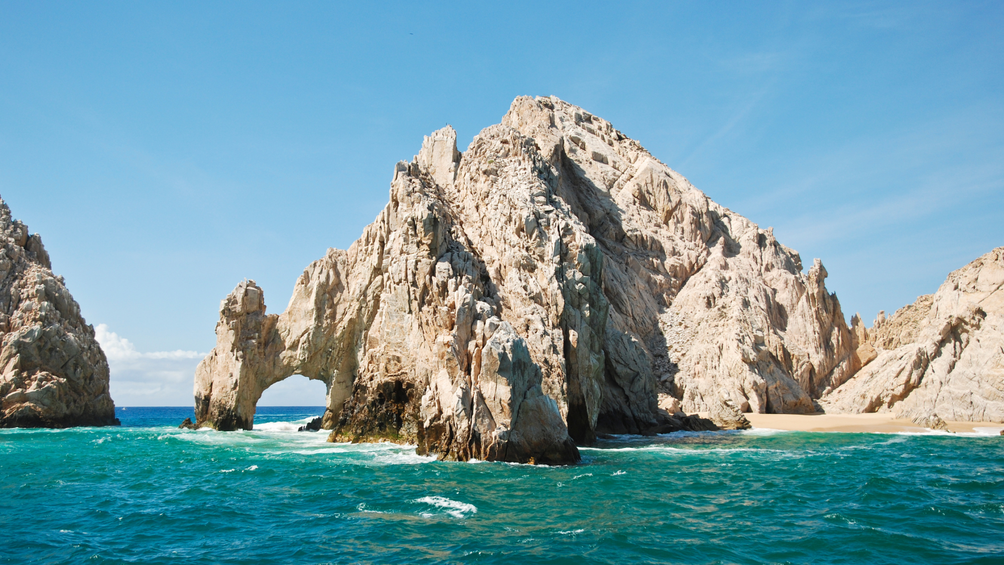 The iconic Arch of Cabo San Lucas, a natural rock formation at Land's End with clear blue ocean waves surrounding it.