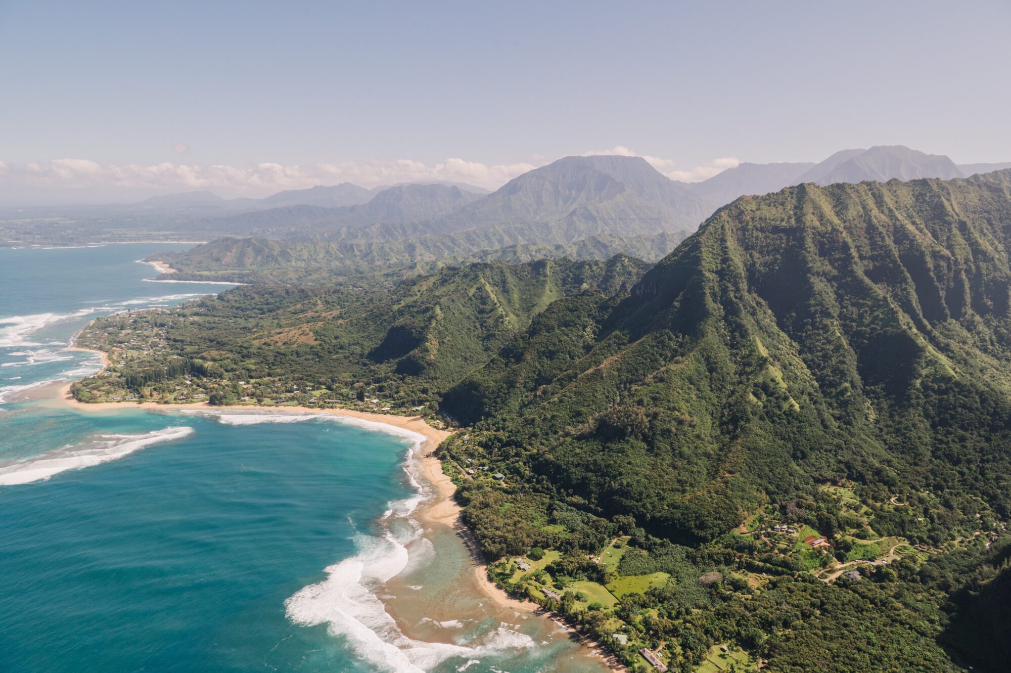 Stunning aerial view of the rugged Napali Coast on Kauai, Hawaii, showcasing dramatic green cliffs, deep valleys, and the blue Pacific Ocean meeting the shoreline.