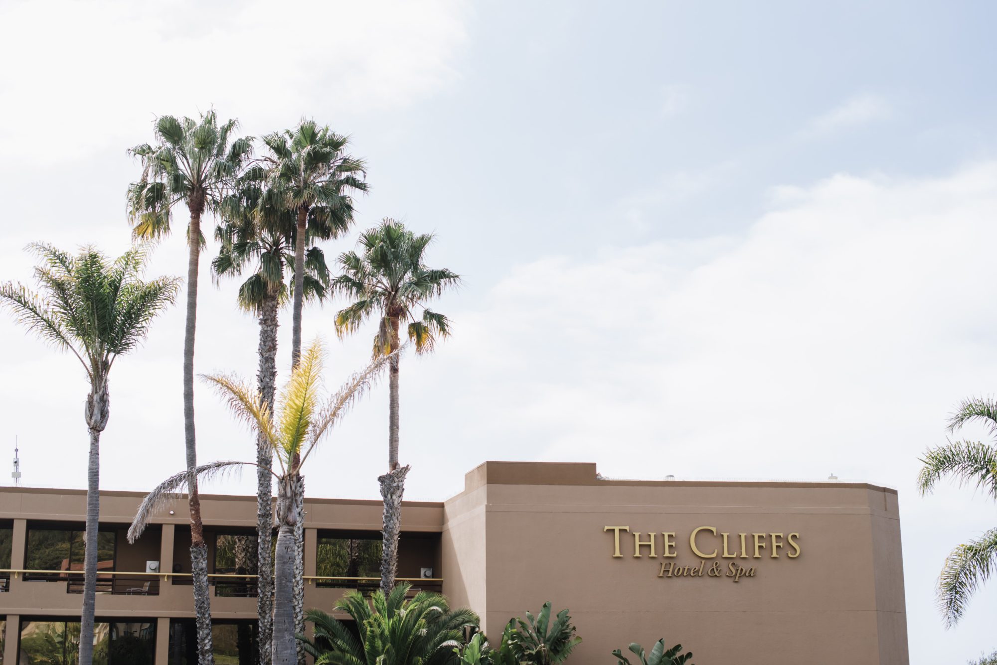 Brown building that says "The Cliffs Hotel and Spa". Palm trees are in front of building. 