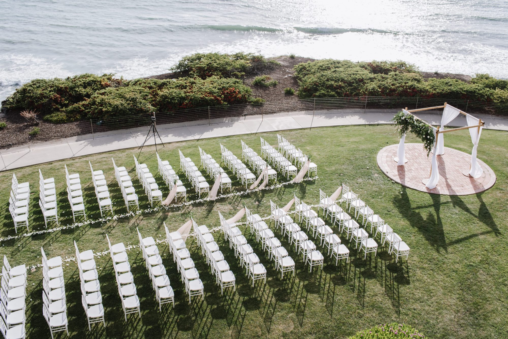 Wedding ceremony venue. White chairs are lined up in front of a wedding arbor with white drapery and flowers.